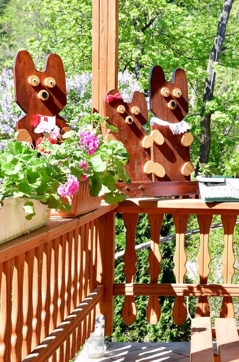Drewniane figurki misiów na balustradzie tarasu, obok pelargonie